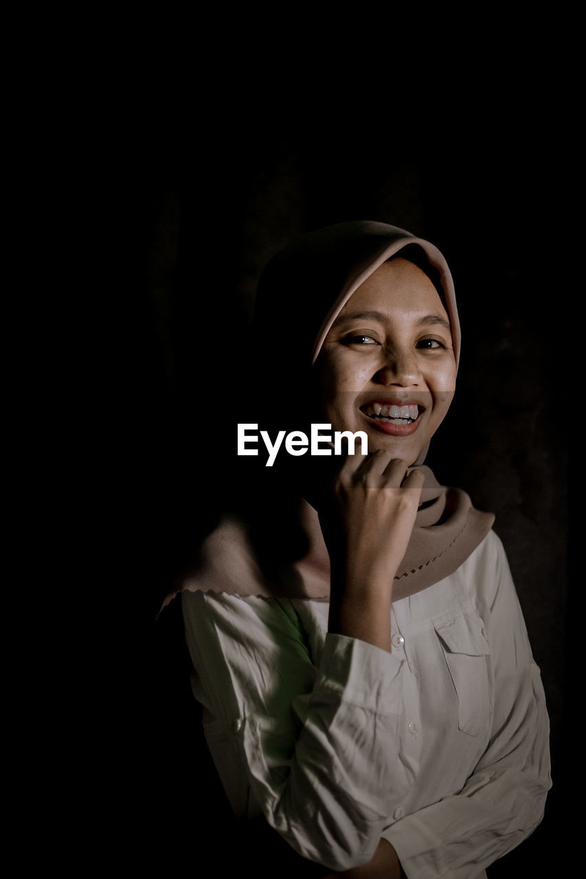 Portrait of a smiling young woman against black background