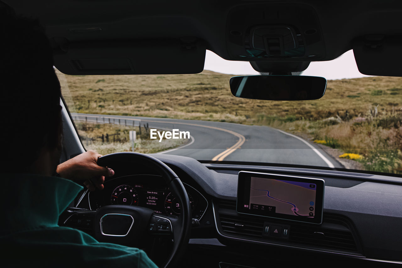 Unrecognizable man driving a car on an empty countryside road, view from the inside of the car