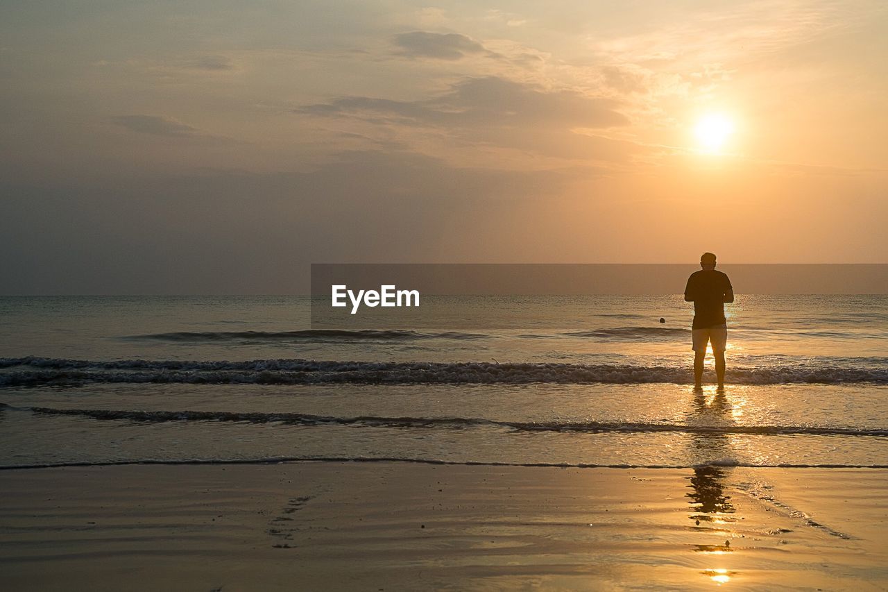 SILHOUETTE MAN STANDING ON BEACH AGAINST SKY DURING SUNSET