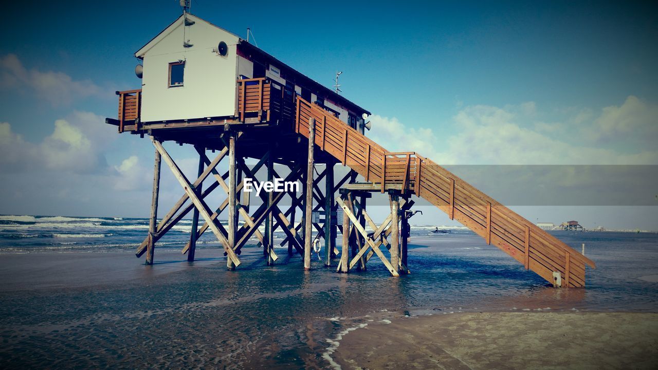 Stilt house at beach against sky