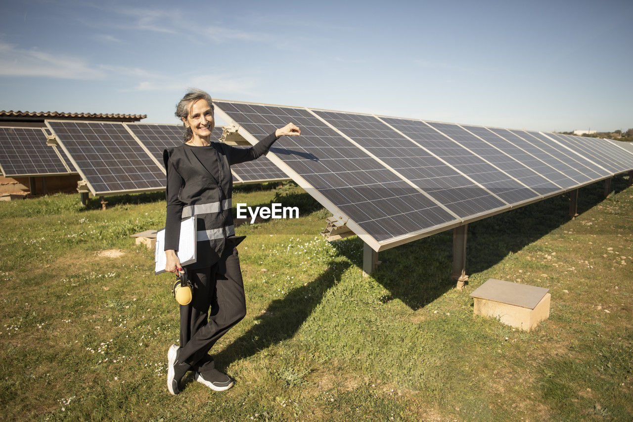 Portrait of smiling senior female engineer standing near solar panels at power station