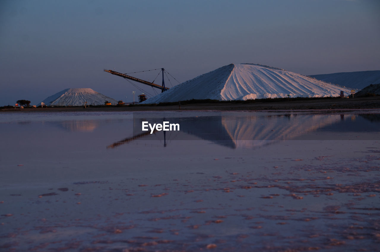 Scenic view of lake by salt mountains against clear sky at dusk