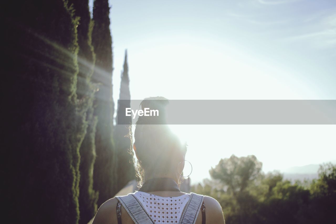 Rear view of woman by trees against sky on sunny day