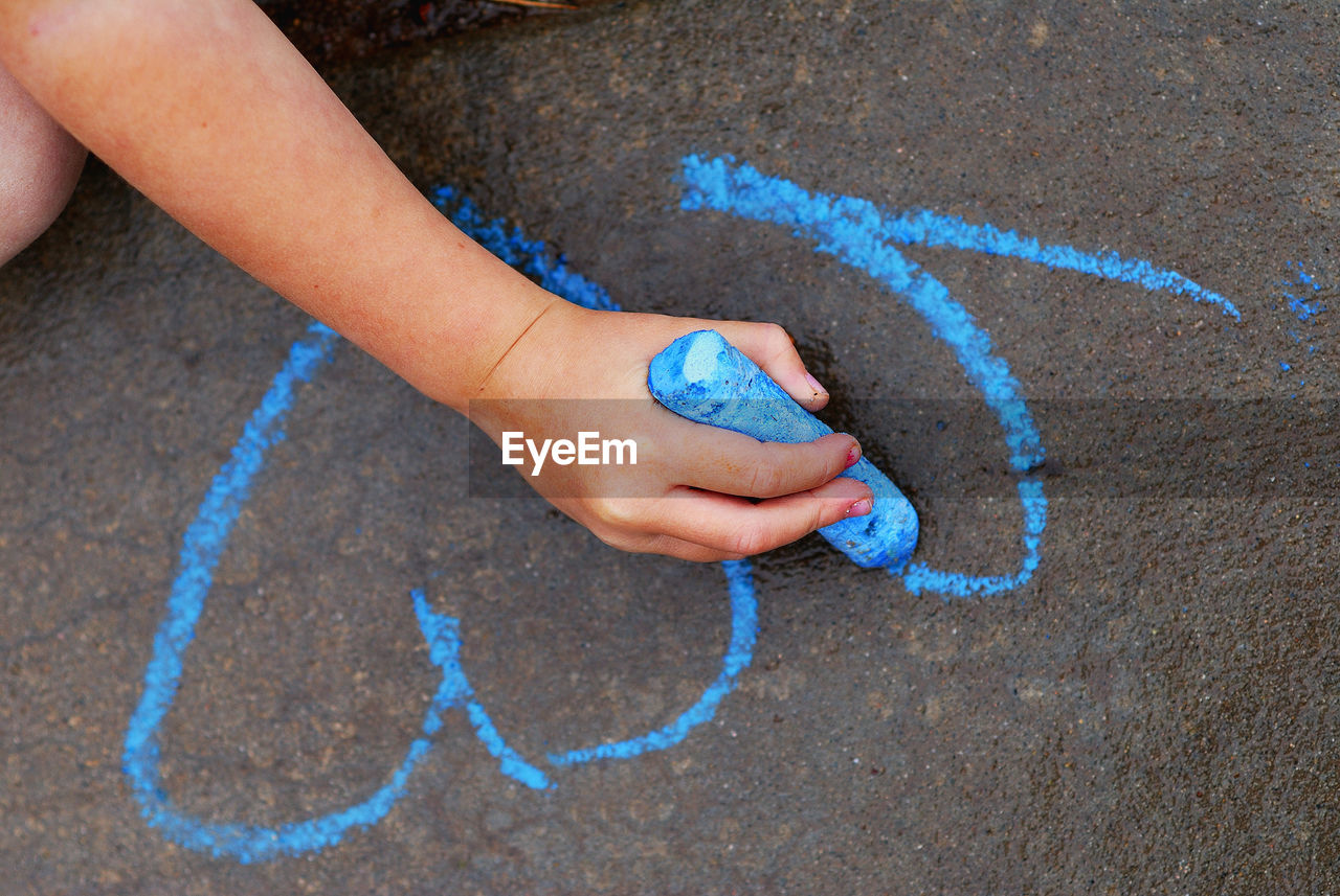 Cropped hand of girl drawing on road