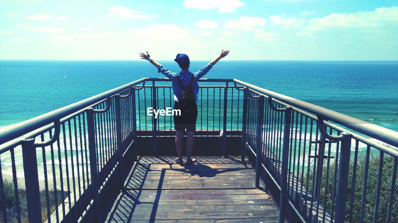Rear view of woman with arms raised standing at observation point against sea
