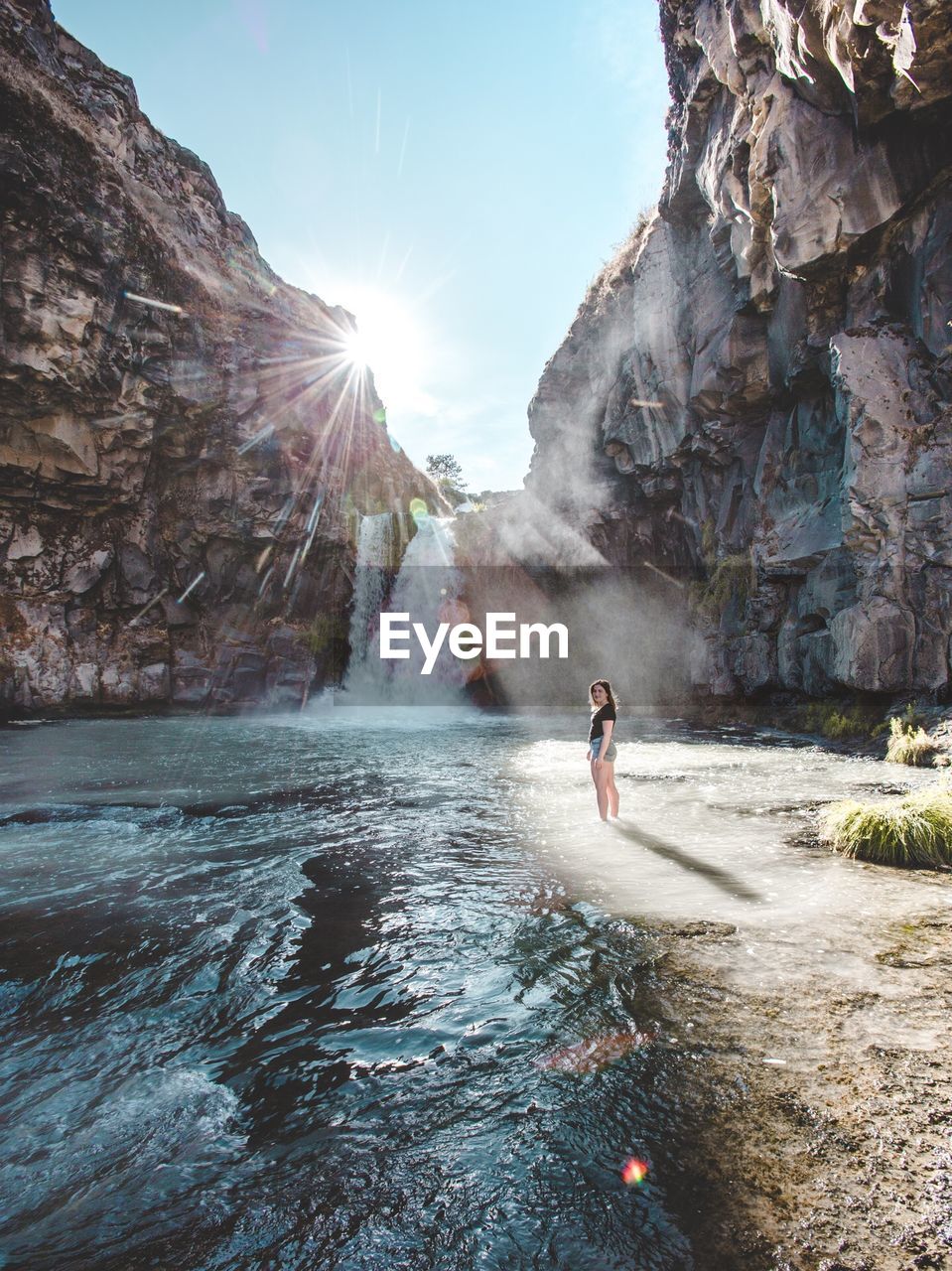 Woman standing in river against waterfall in sunny day