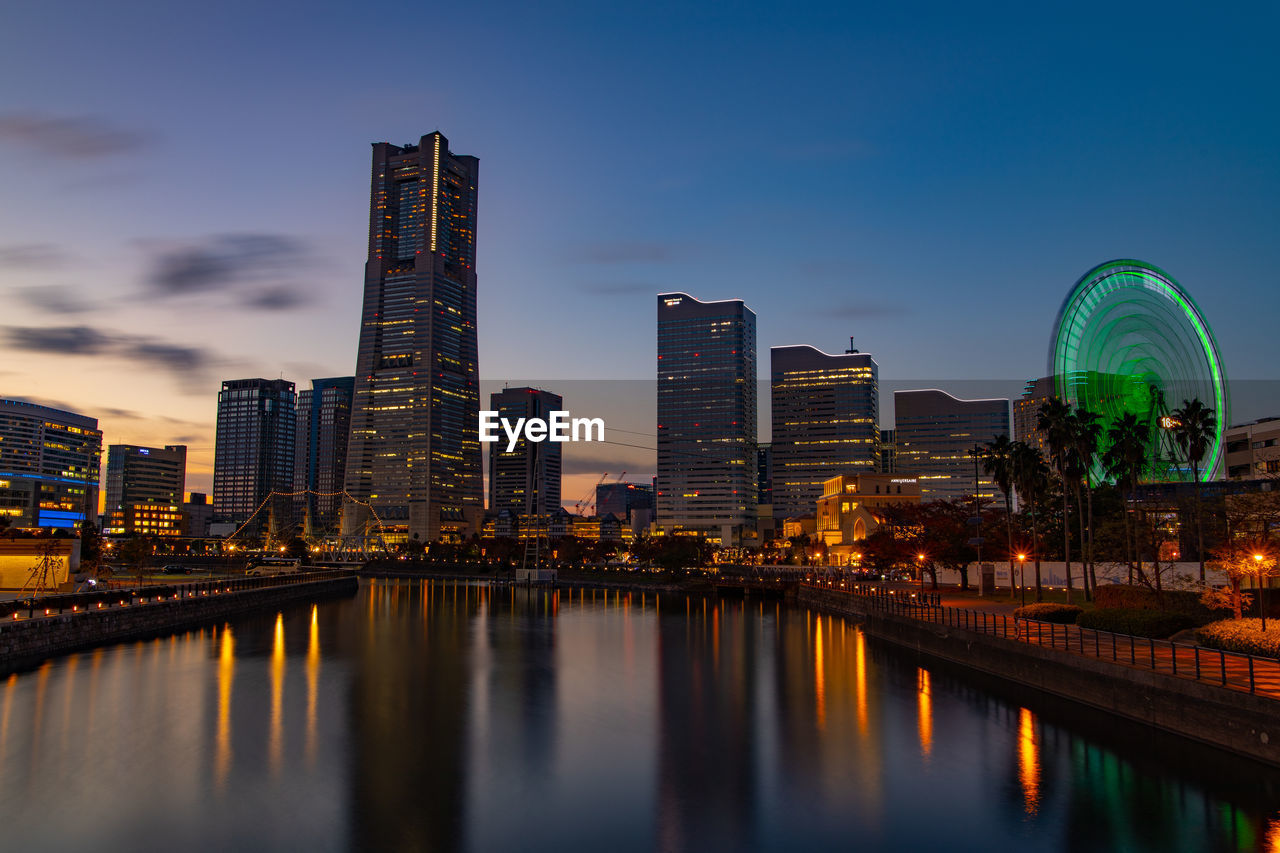 Illuminated buildings by river against sky in city