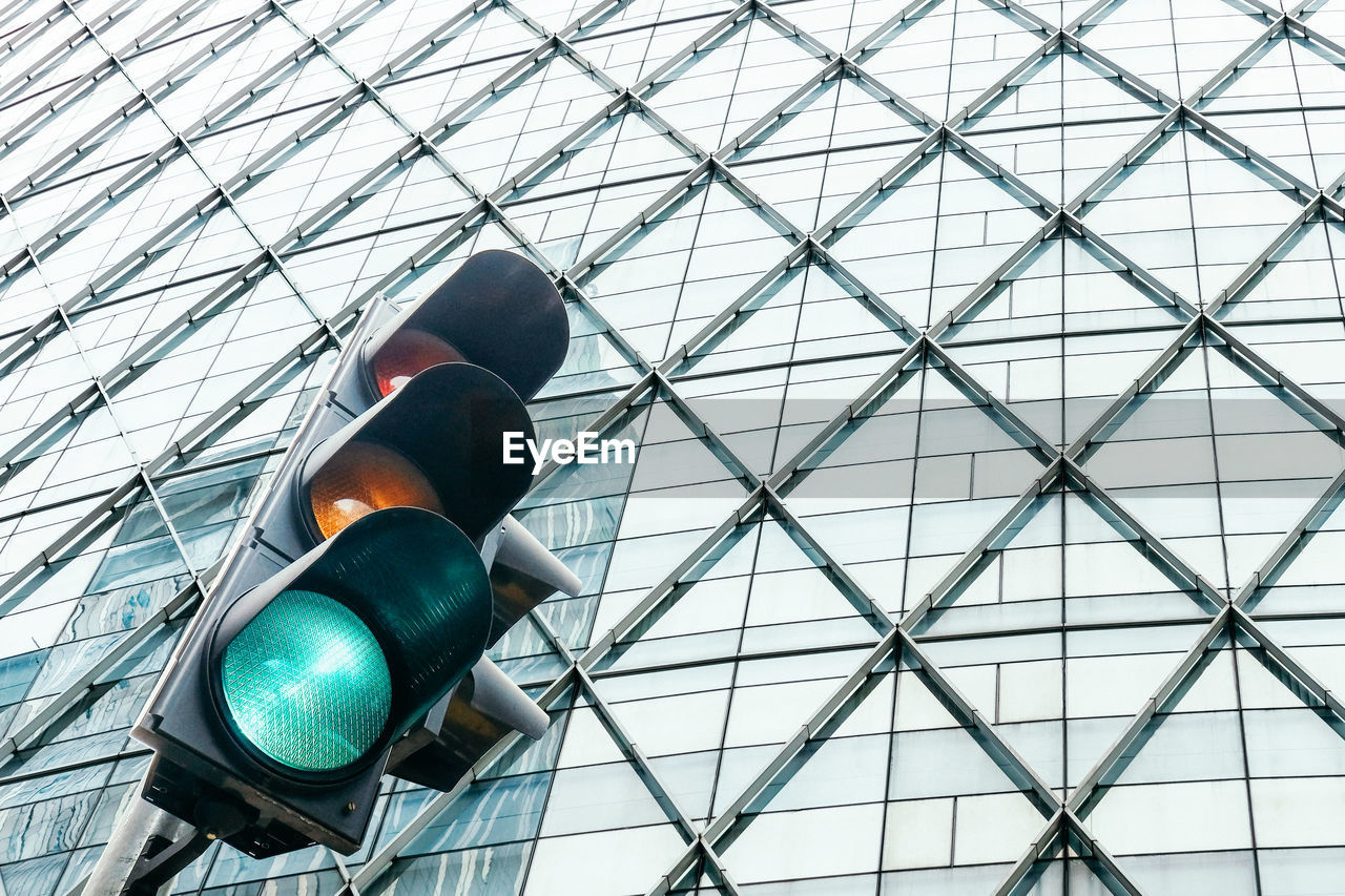 Low angle view of traffic lights against glass building in the city