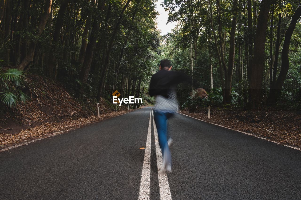 Full length rear view of man running on road in forest