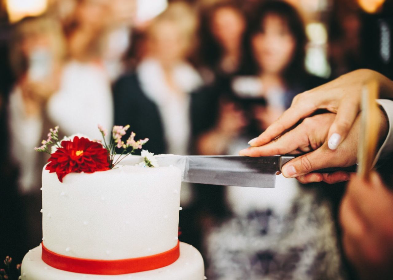 Close-up of hands cutting wedding cake