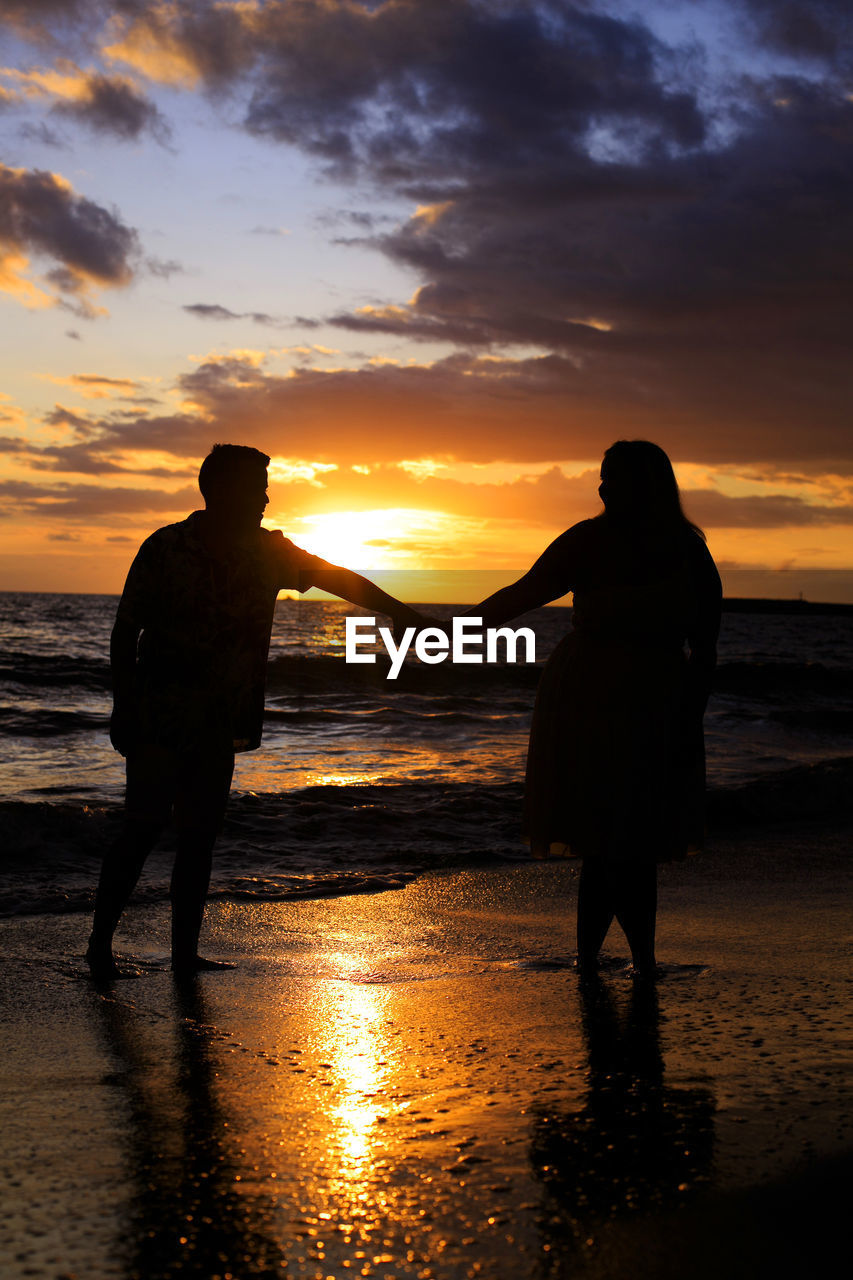 A young couple walking on the beach at sunset