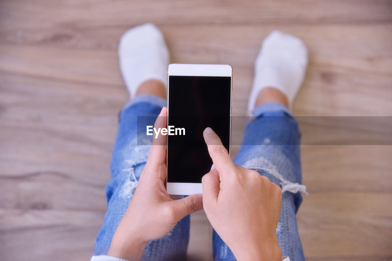 Low section of woman using mobile phone on hardwood floor