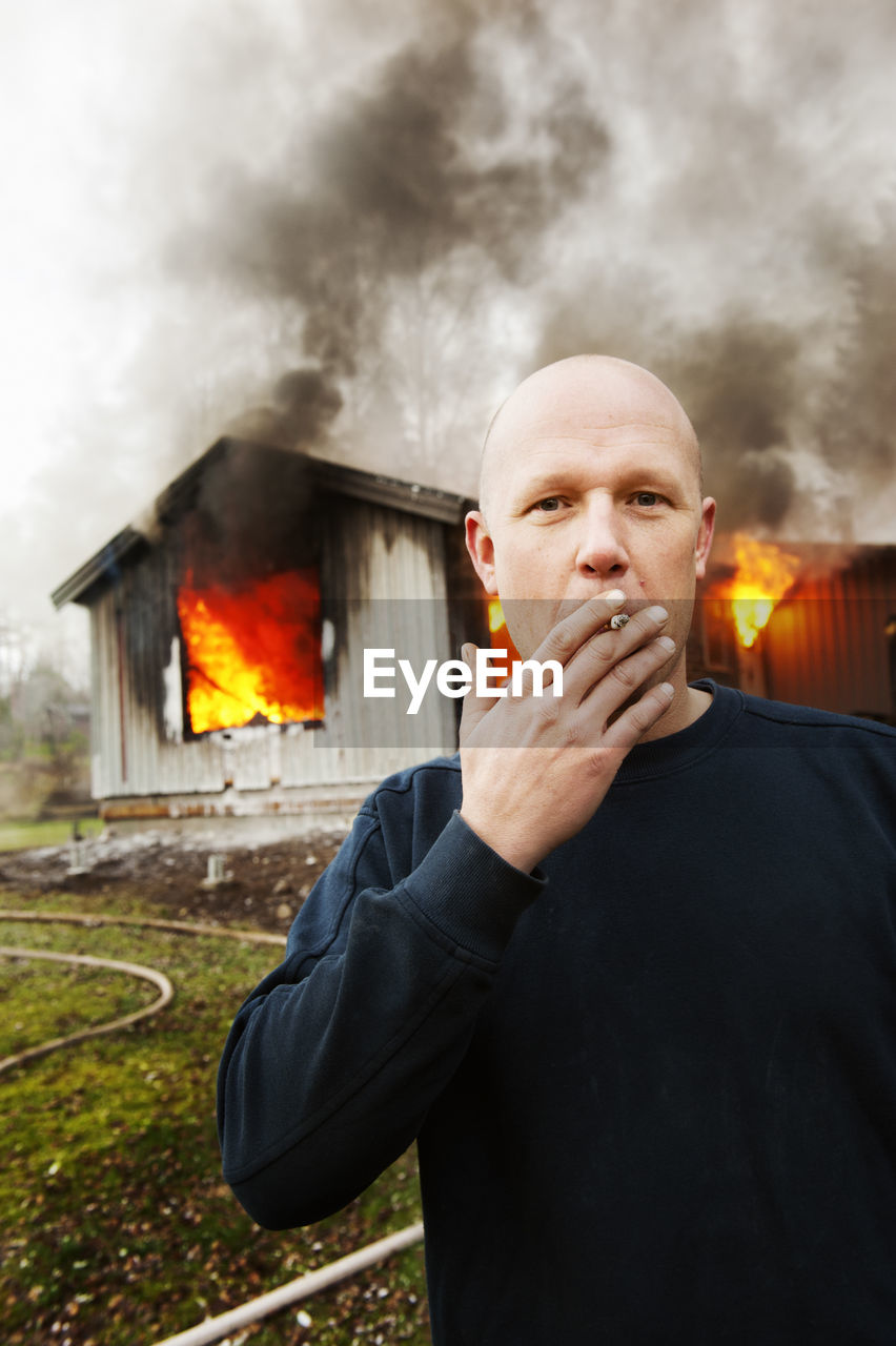 Man smoking cigarette in front of burning building