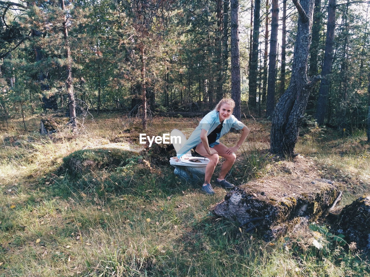 Woman in chair position over abandoned toilet seat in forest