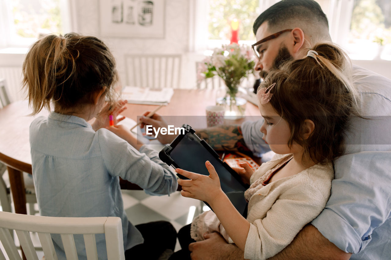 Girl using digital tablet while father assisting daughter in homework at dining table