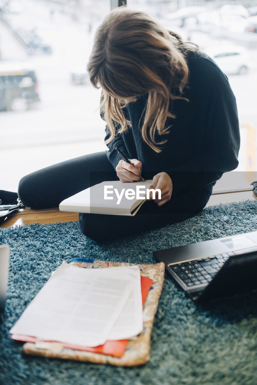 High angle view of businesswoman writing on notepad while sitting at office cafeteria