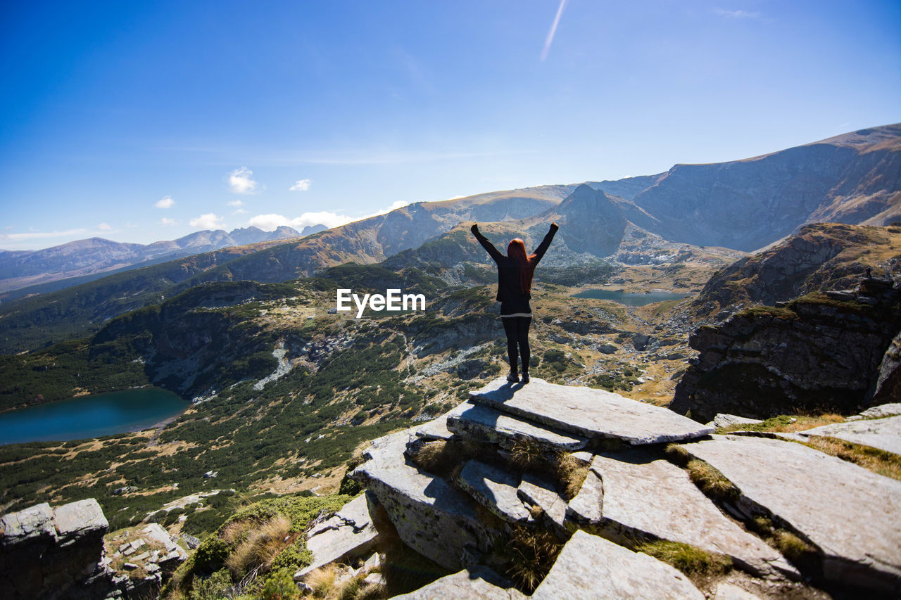 Rear view of young woman with arms raised standing on mountain against sky