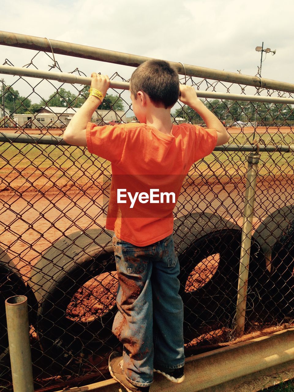 Full length rear view of boy standing on chainlink fence