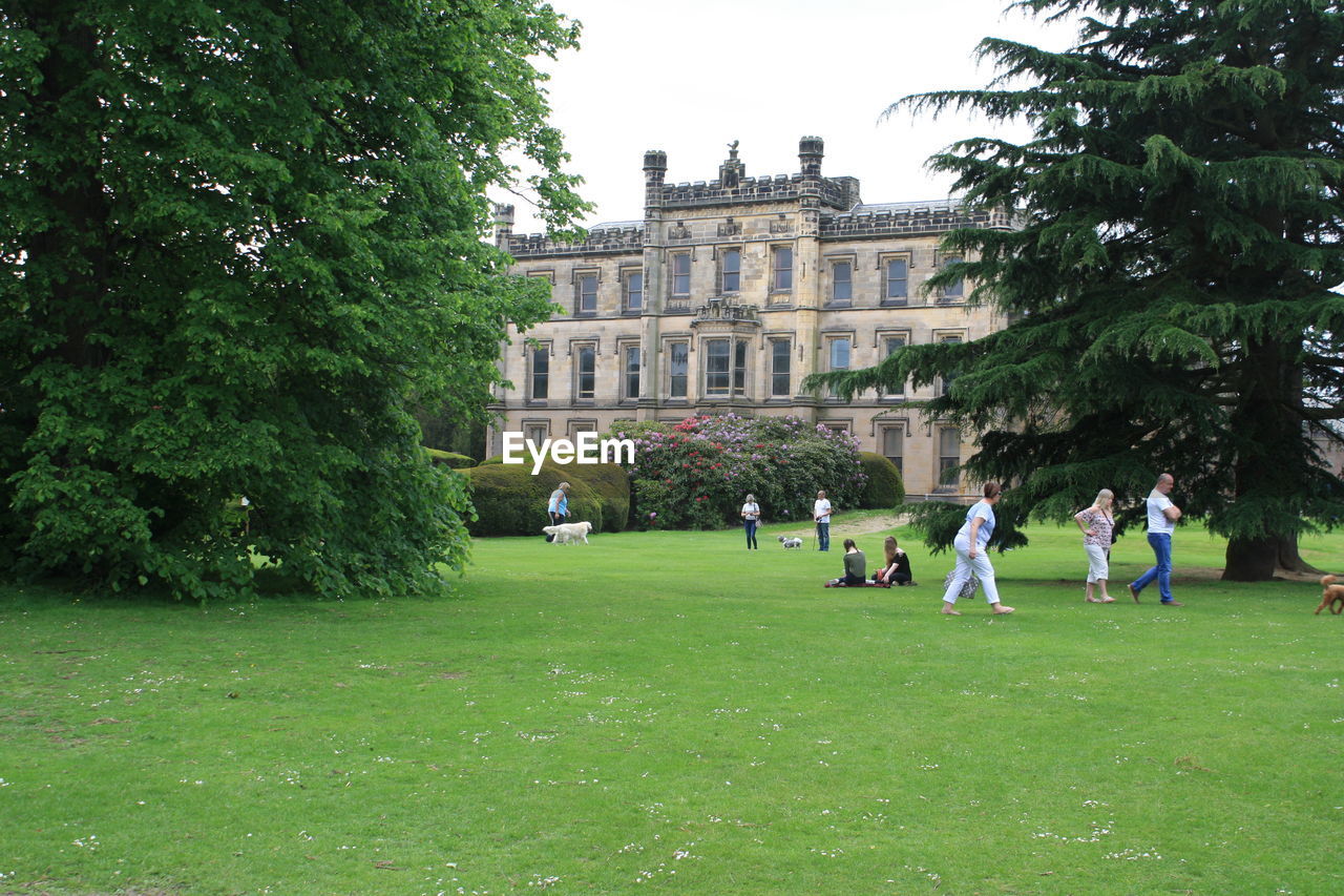 PEOPLE IN FRONT OF BUILT STRUCTURE AGAINST TREES