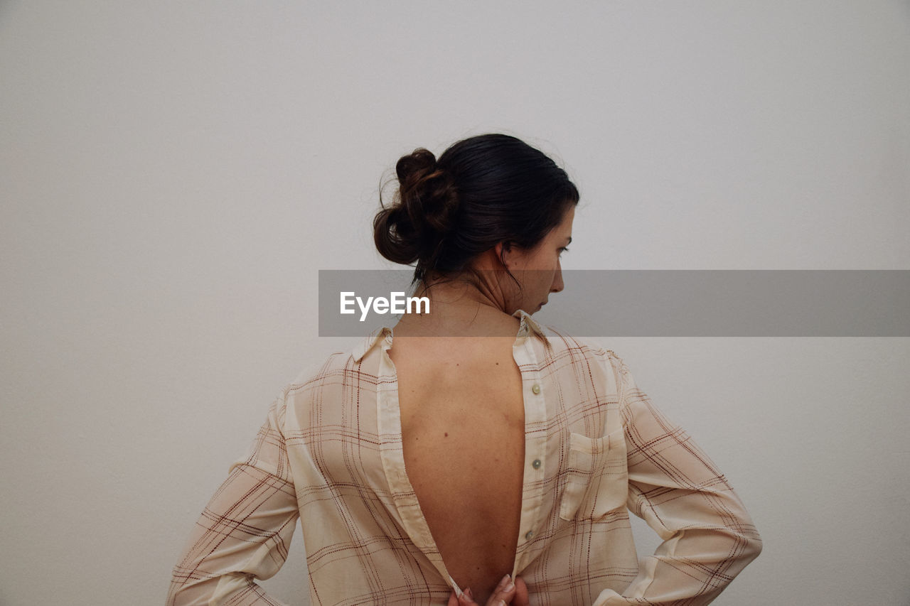 Rear view of woman buttoning shirt against white background