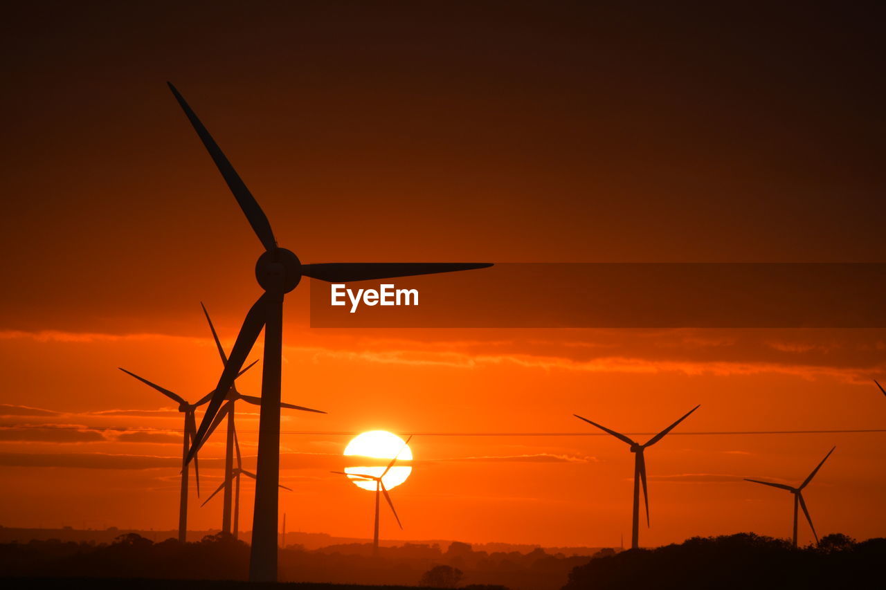 A bright red sunset through wind turbines