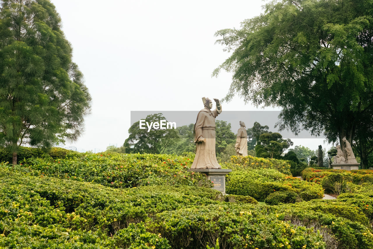 Statue against trees and plants against sky