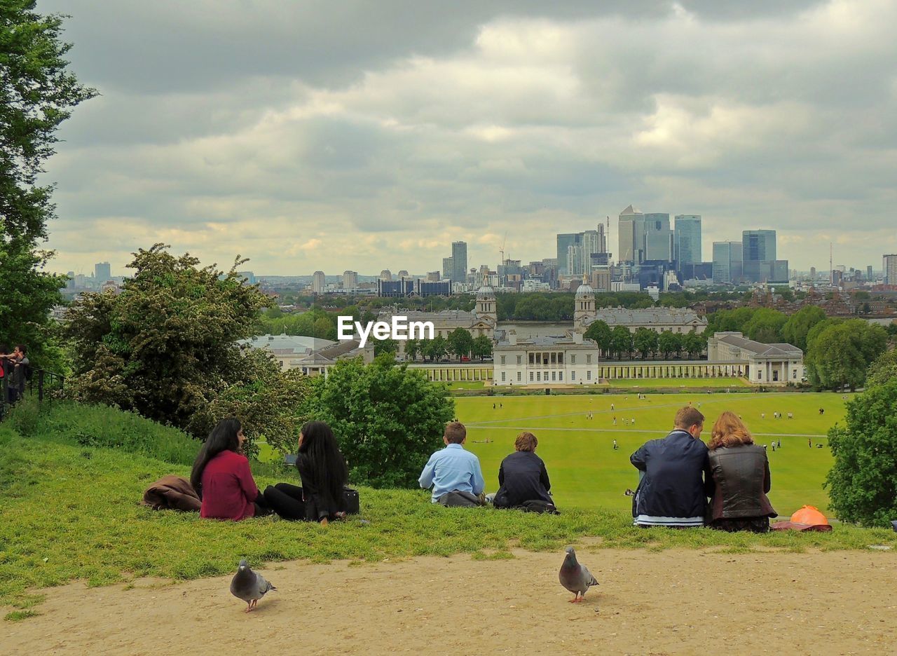 PEOPLE SITTING IN CITY AGAINST CLOUDY SKY