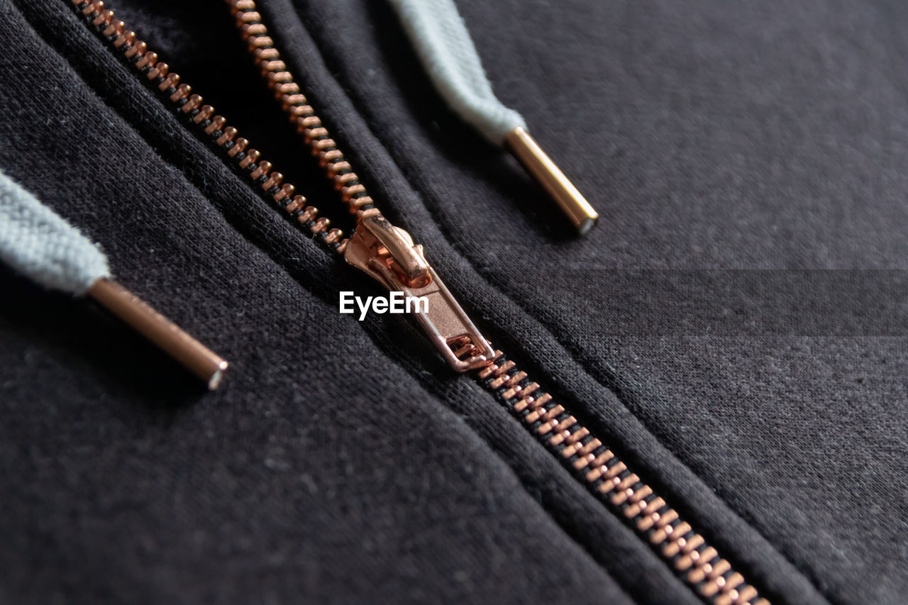 Copper colored fashion zipper in close-up macro view showing black sweatshirt with opened zipper