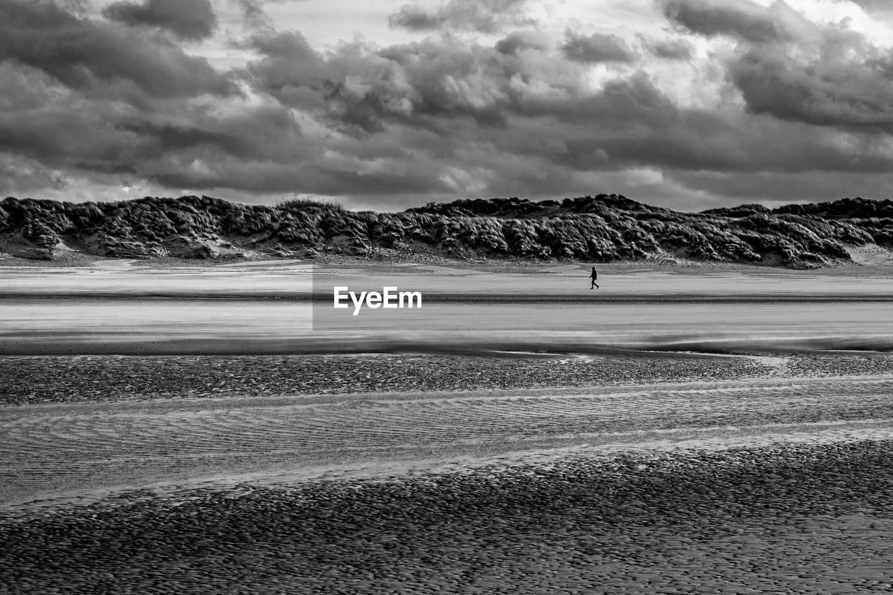 Single person walking alone at a windy beach at bray-dunes in france