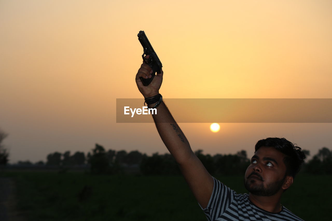 MAN WITH ARMS OUTSTRETCHED AGAINST SKY DURING SUNSET