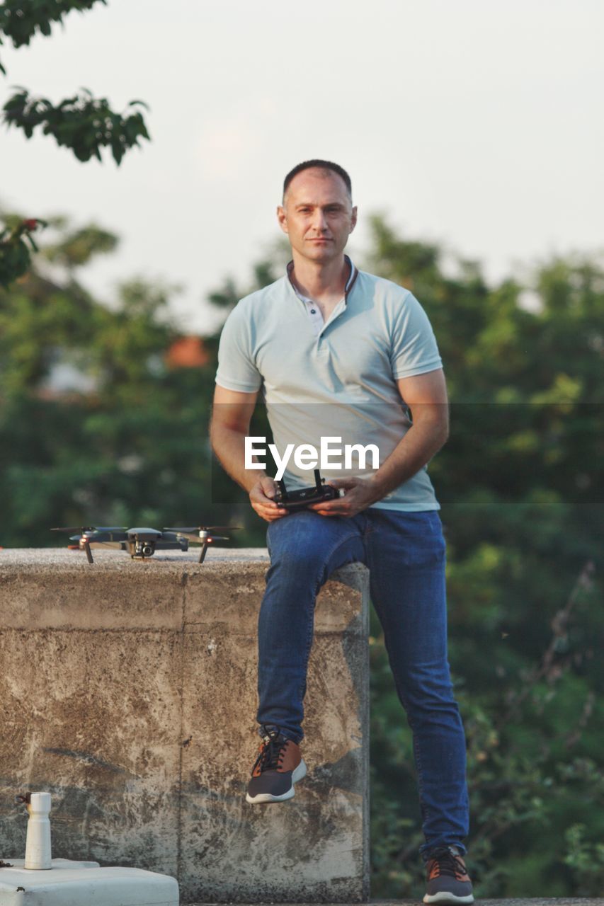 Portrait of man operating drone against sky