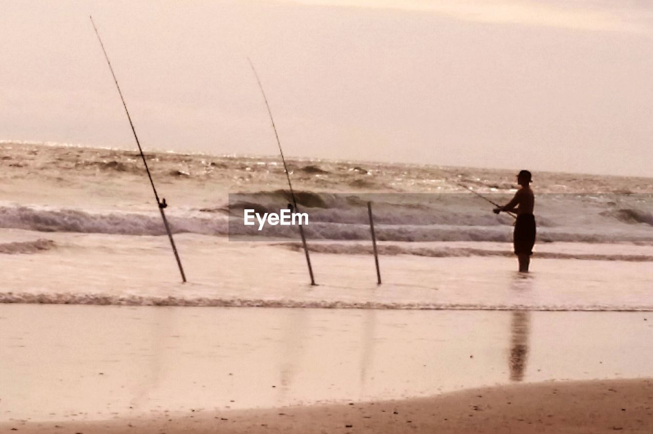 REAR VIEW OF MAN STANDING ON BEACH