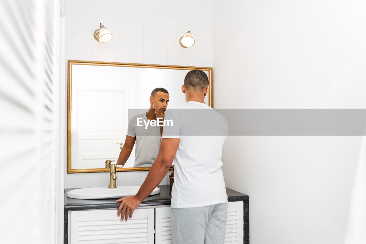 Rear view of young man looking in mirror at home