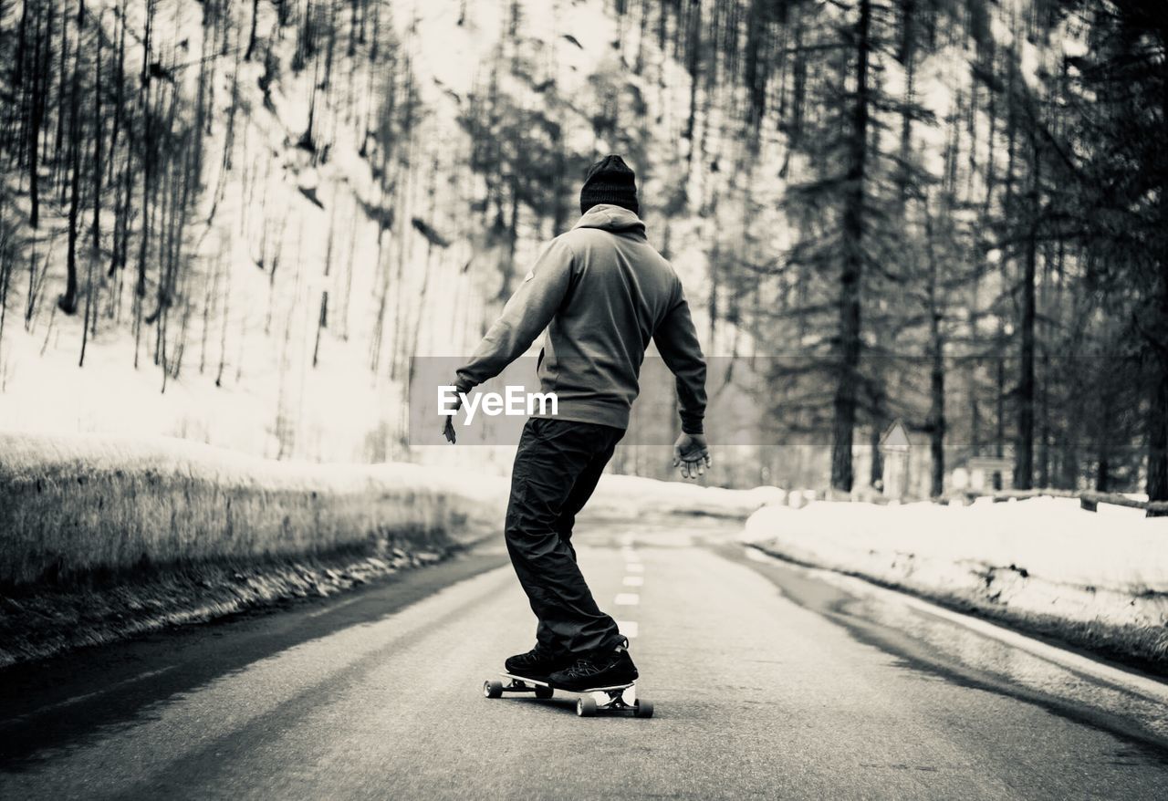 Rear view of man skateboarding on road during winter