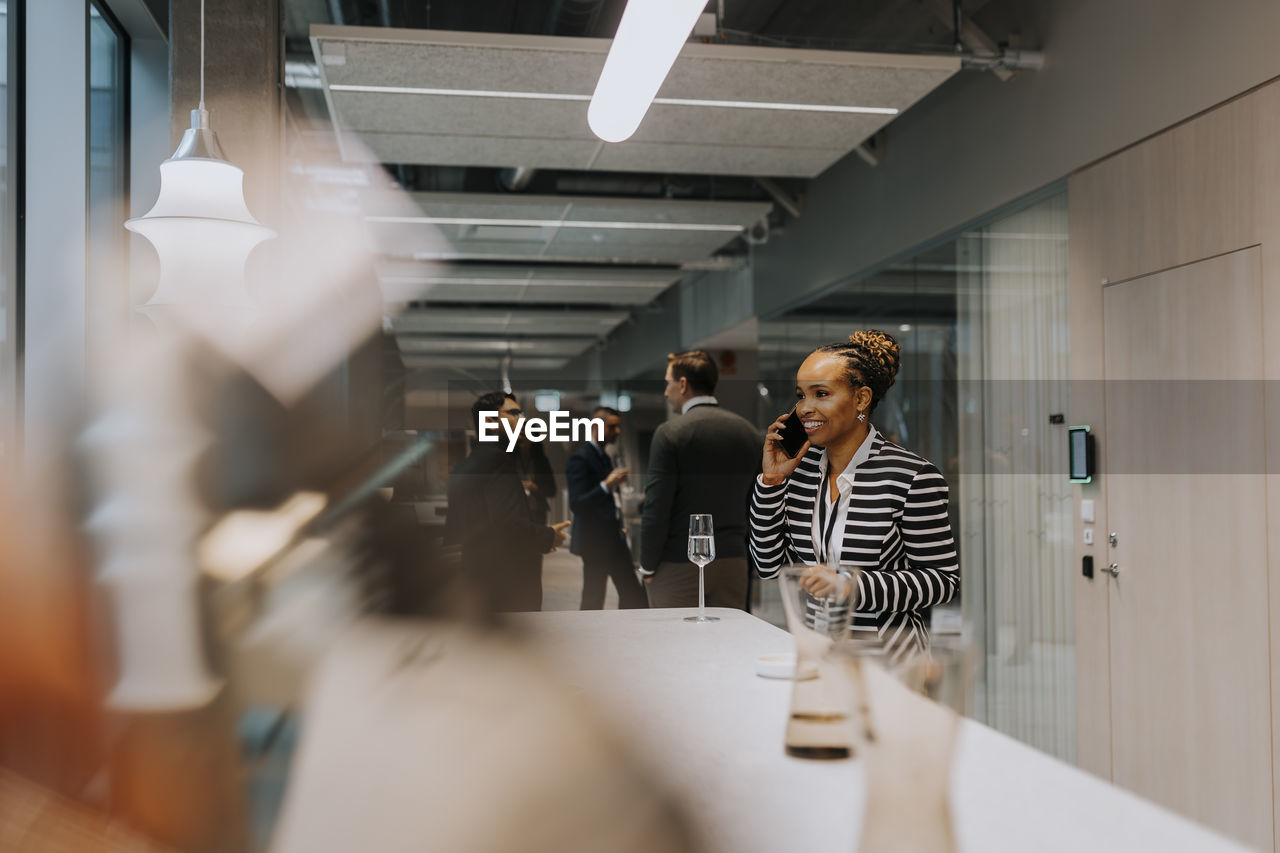 Smiling mature businesswoman talking on mobile phone while standing by table in conference