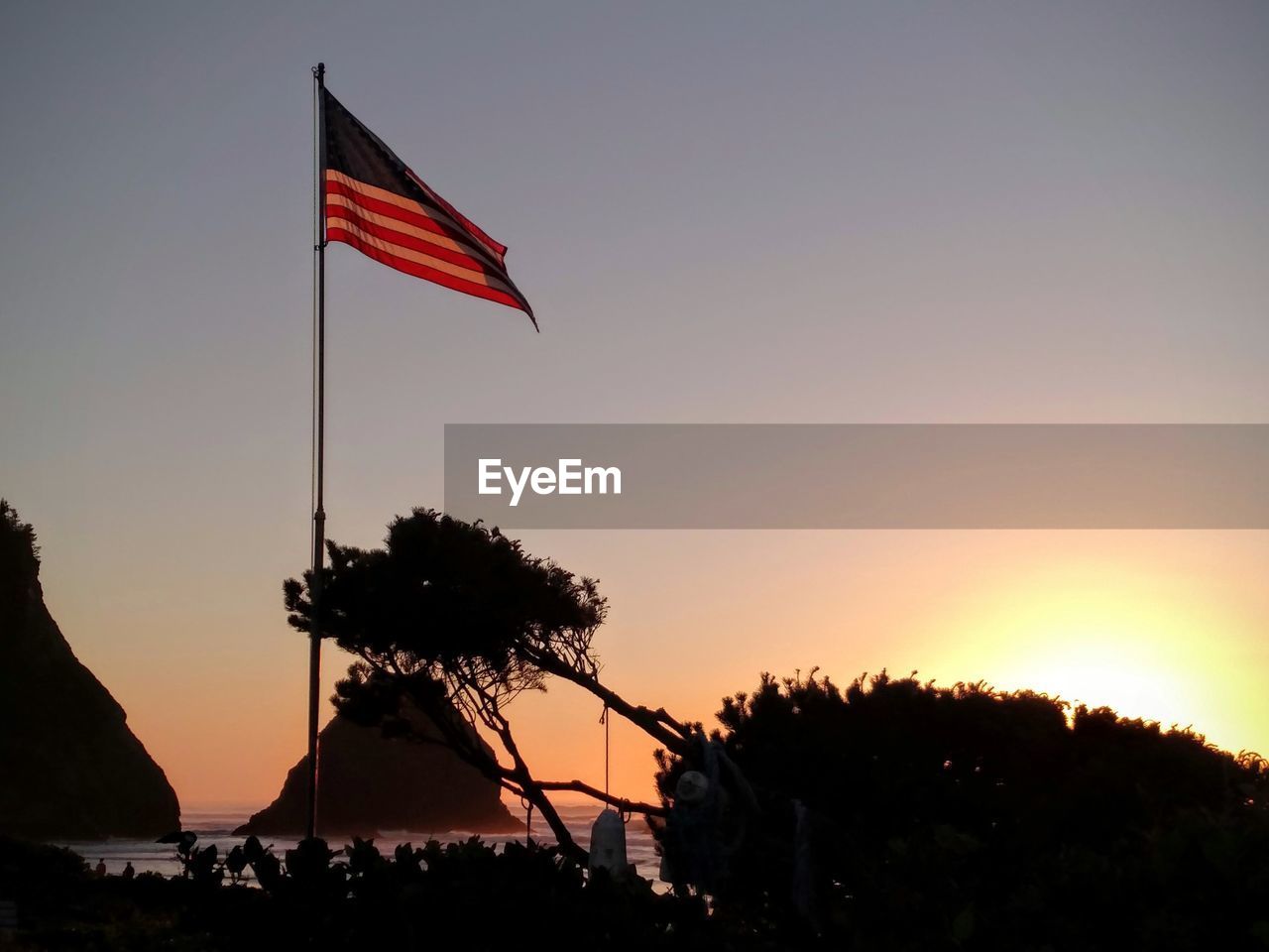 SILHOUETTE OF FLAGS AGAINST SKY DURING SUNSET