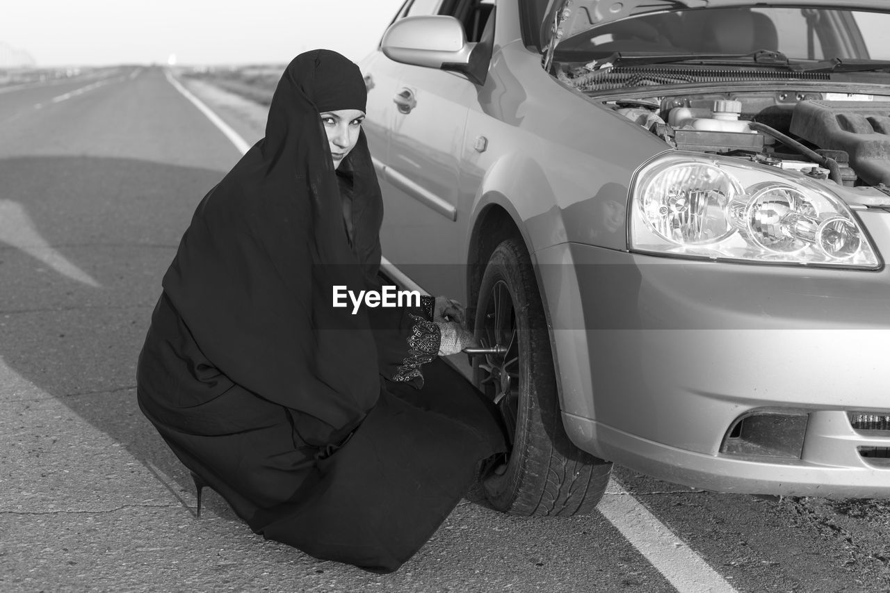 Portrait of woman in burka replacing tire on road