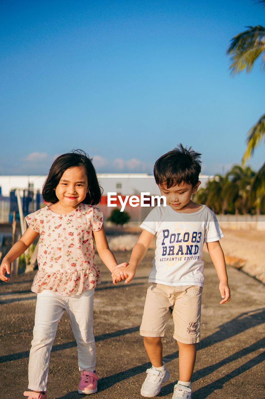 Full length of siblings holding hands walking on street