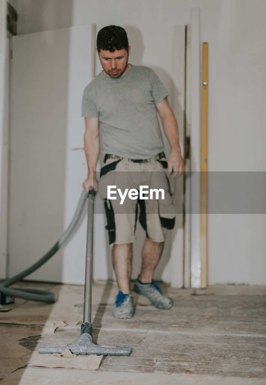 A young man vacuums the floor with a construction vacuum cleaner.