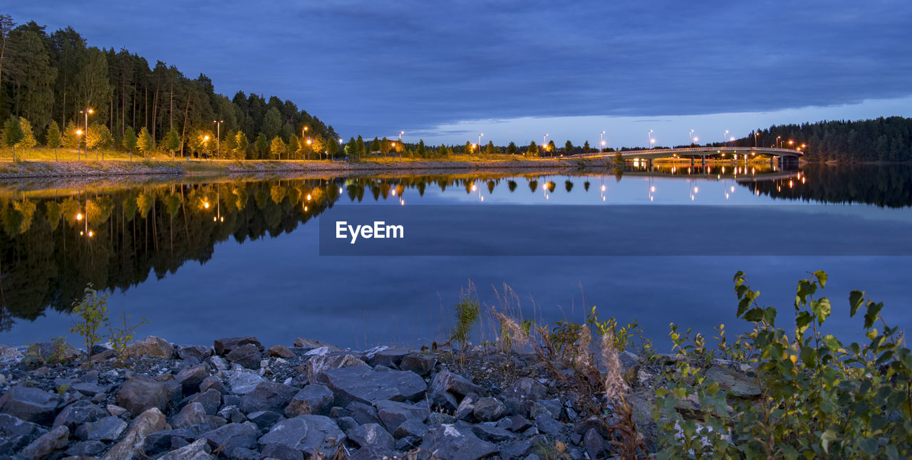 Illuminated street lights reflecting on lake against blue sky