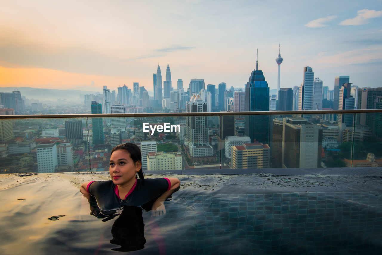 Thoughtful woman in infinity pool against city
