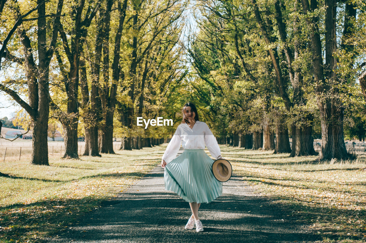 Portrait of woman standing on road amidst trees