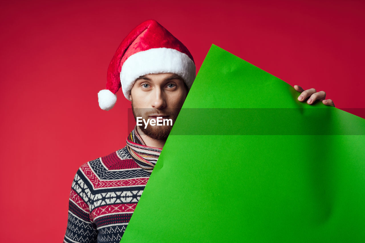 one person, portrait, red, green, studio shot, adult, colored background, beard, facial hair, christmas, indoors, men, celebration, hat, santa hat, looking at camera, young adult, emotion, holiday, fun, clothing, humor, person, happiness, copy space, headshot