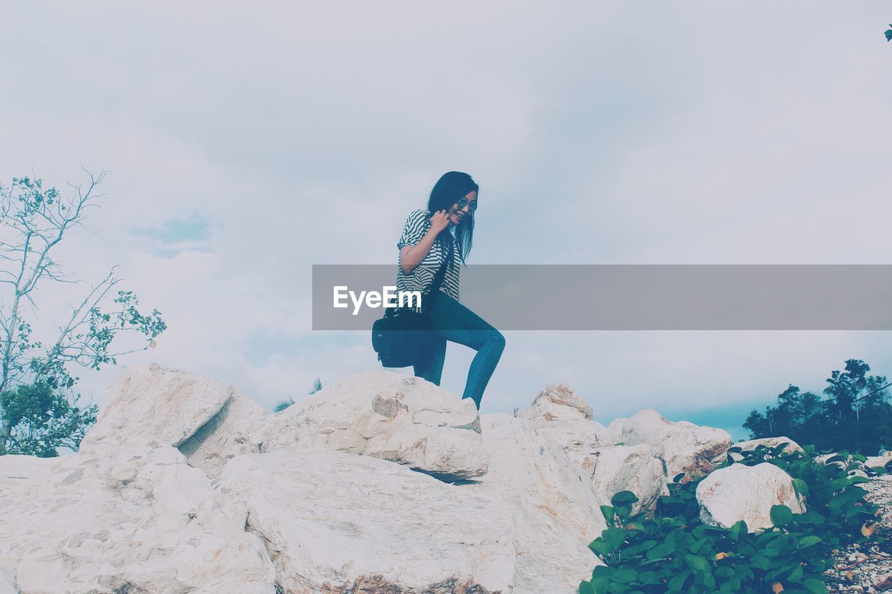 Low angle view of woman standing on rocks against cloudy sky