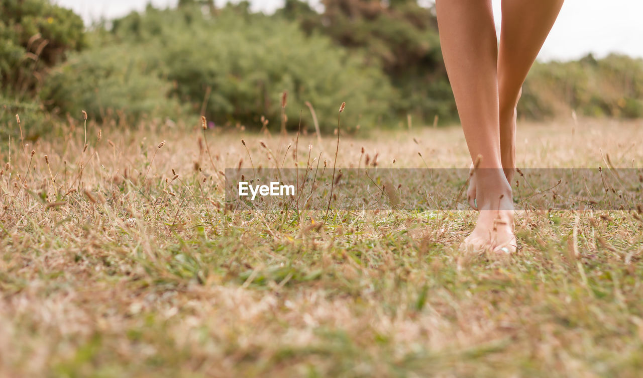 LOW SECTION OF WOMAN STANDING ON FIELD BY WATER