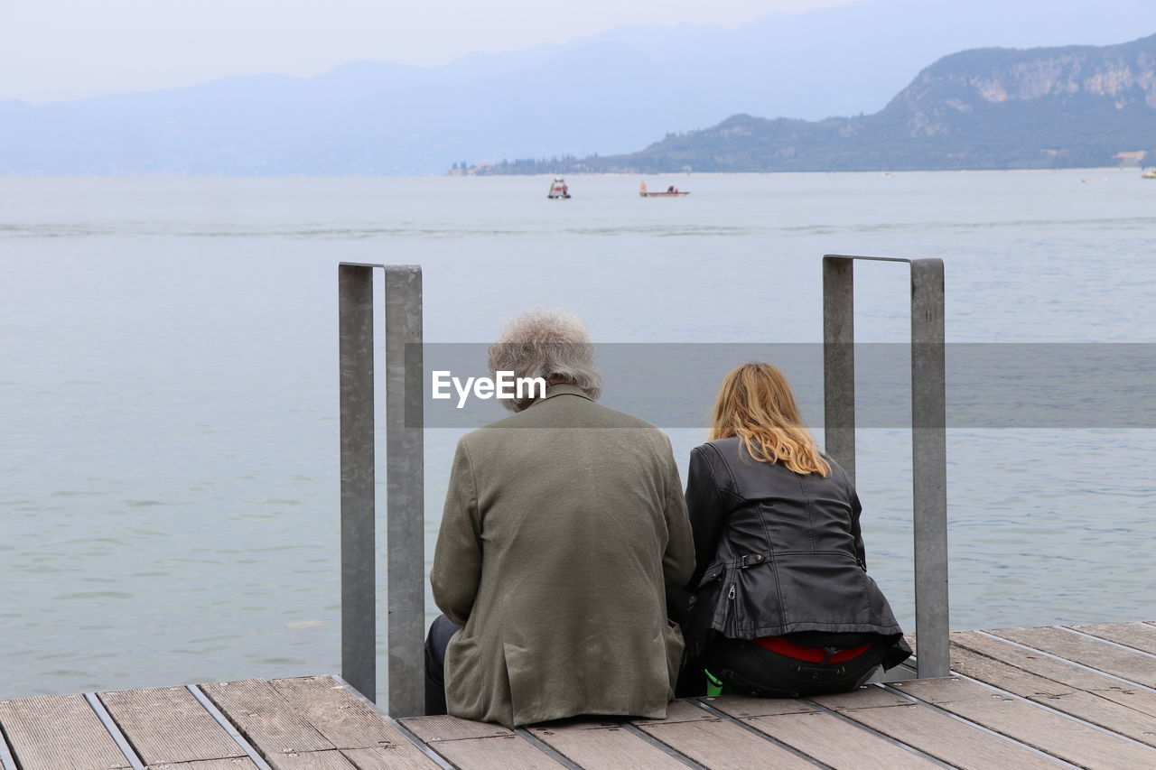 REAR VIEW OF PEOPLE SITTING ON PIER