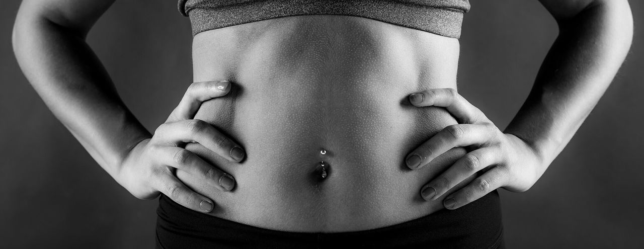Midsection of woman hand on hip with belly button ring