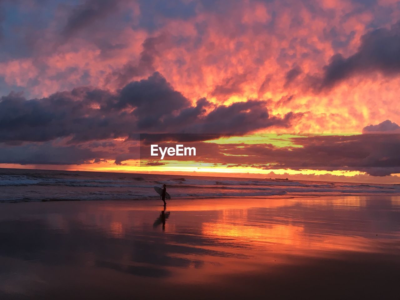 Silhouette man with surfboard standing at beach against sky during sunset