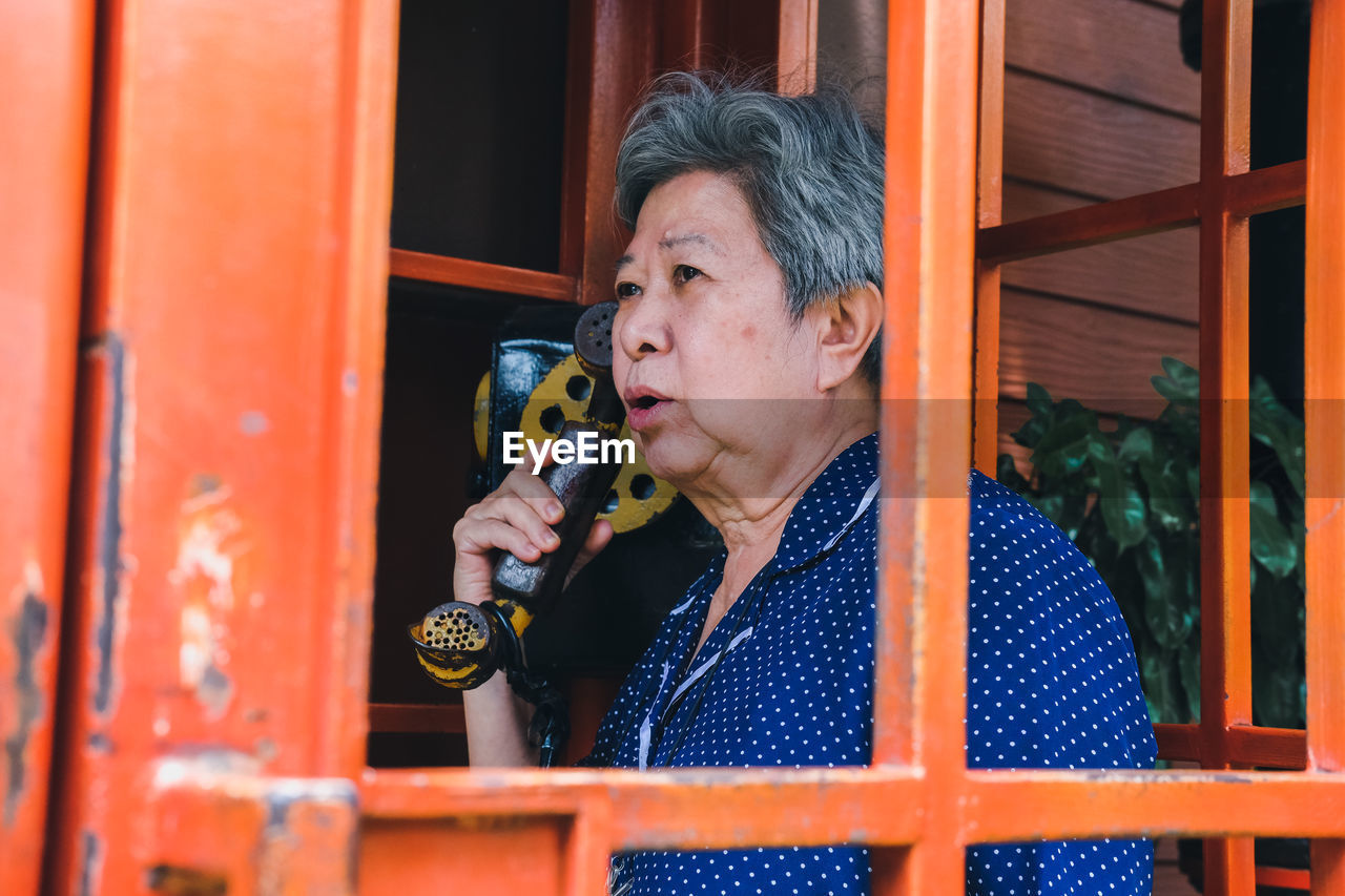 Senior woman talking on phone in telephone booth