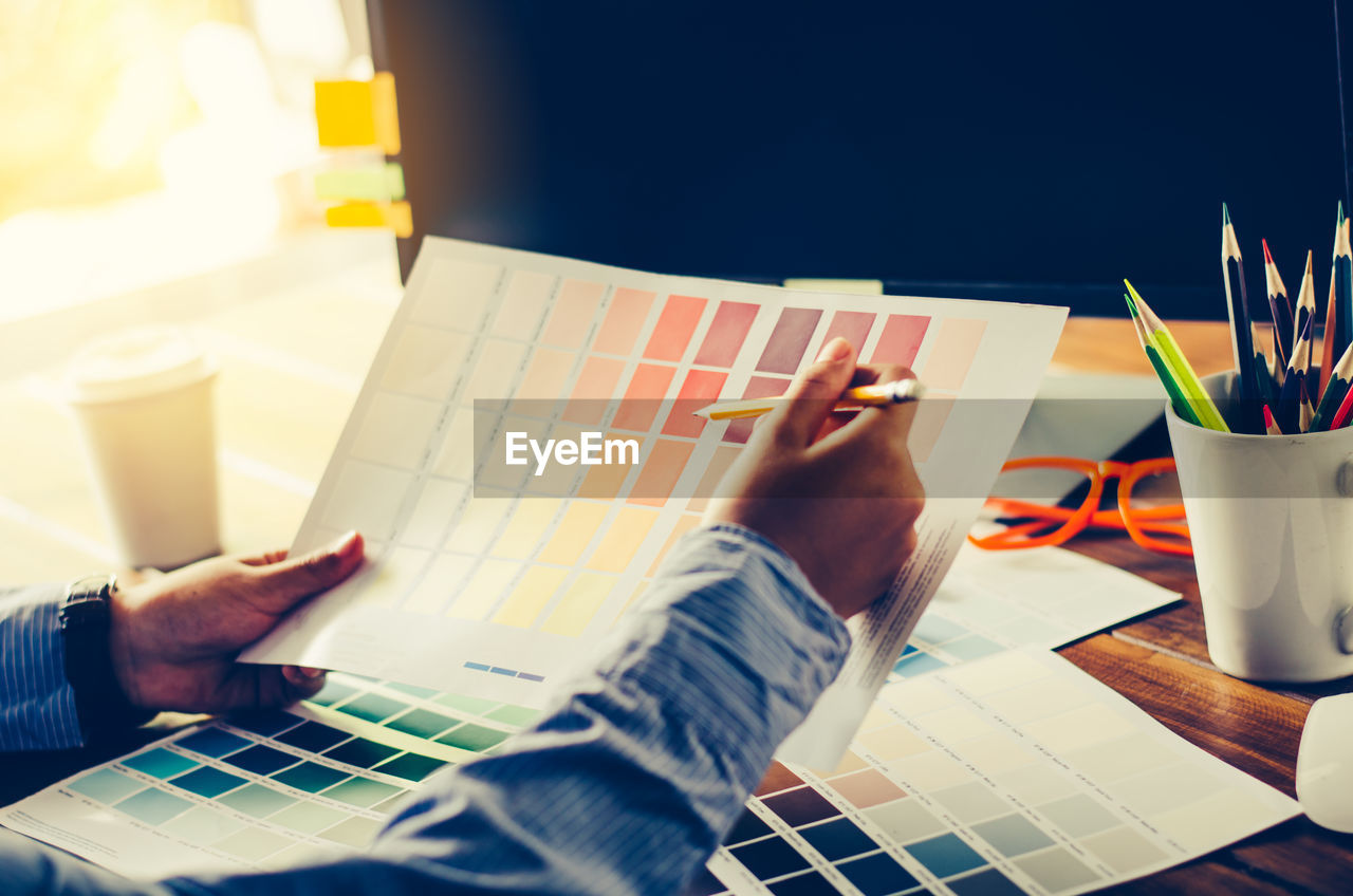 Cropped hands of businessman holding color swatch in office